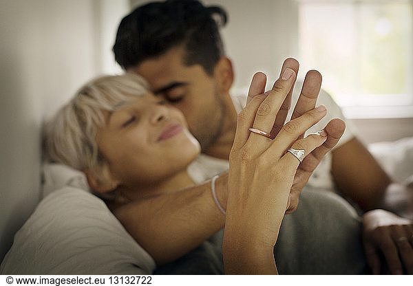 Affectionate young man kissing woman while holding hand in bedroom