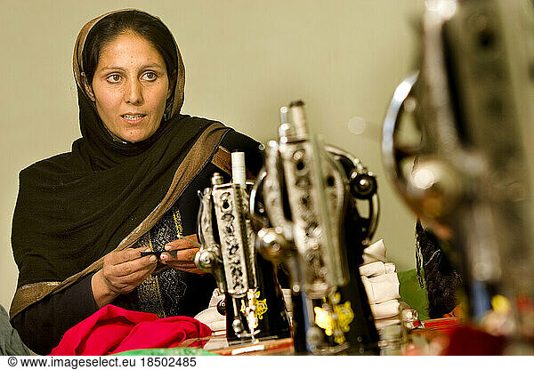 Afghan woman who runs a sewing workshop stands near her sewing machines.