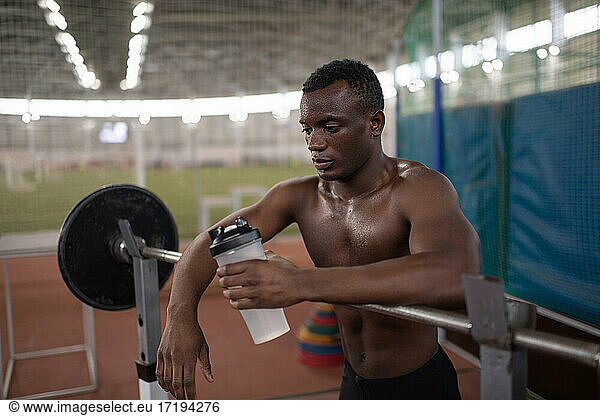African American athlete drinking water near barbell
