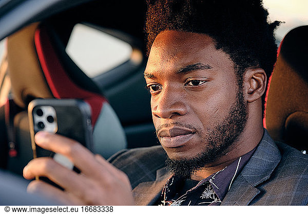 African American Business Man Checking Phone In Sports Car at Sunset