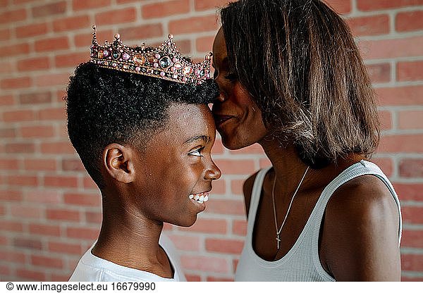 African-American mom kissing forehead of laughing son wearing tiara
