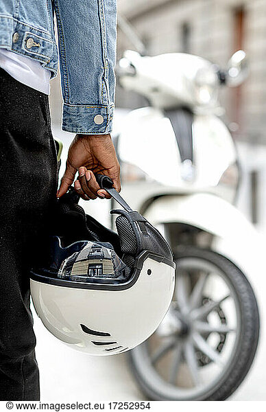African man holding crash helmet while standing by motor scooter