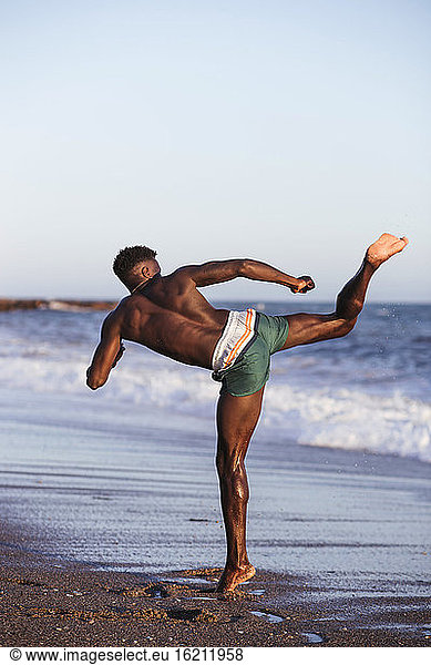 Afrikanischer junger Mann ohne Hemd  der am Strand gegen den klaren Himmel trainiert