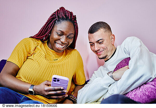 Afro american smiling woman look at mobile with happy friend on sofa