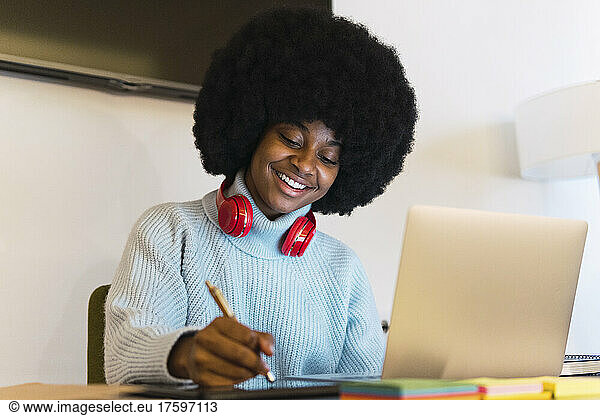 Afro businesswoman using digitized pen on tablet PC at home