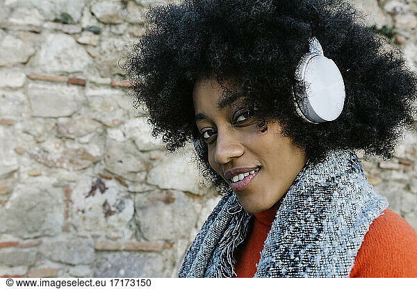 Afro junge Frau hört Musik durch Kopfhörer gegen Steinwand