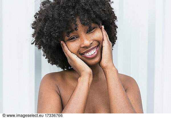 Afro woman with head in hands smiling in front of wall