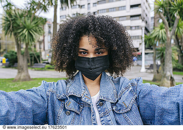 Afro woman with protective face mask taking selfie in city
