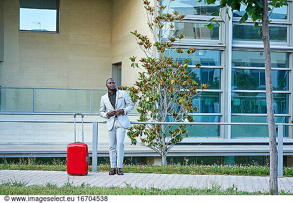 Afroamerikaner in einem weißen Anzug und einem roten Koffer.
