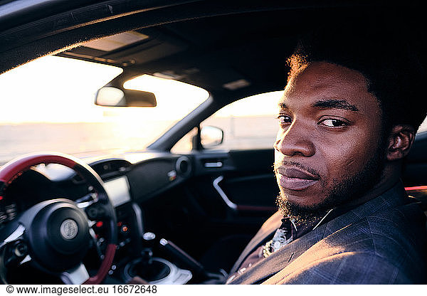 Afroamerikanischer Geschäftsmann im Sportwagen bei Sonnenuntergang