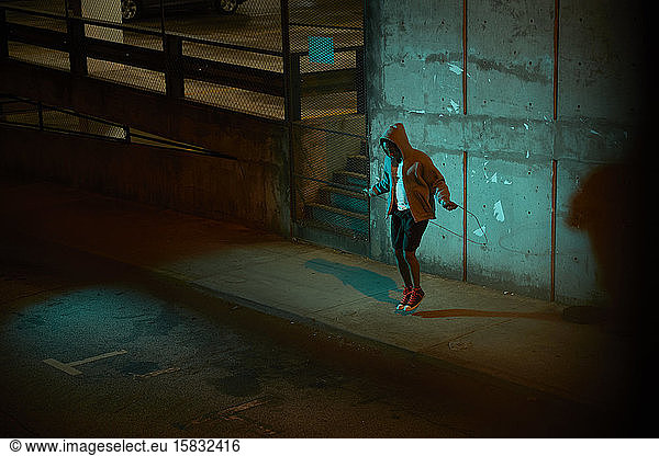 Afroamerikanischer Mann mit Kapuzenpulli trägt nachts Springseil