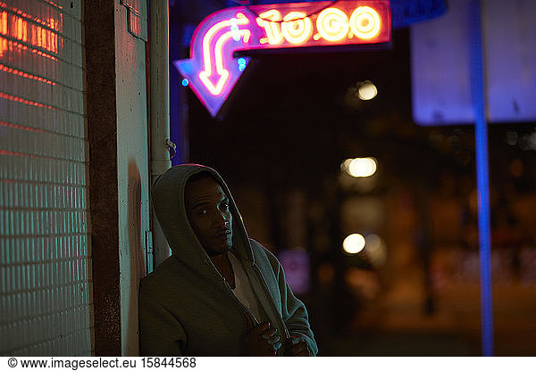 Afroamerikanischer Mann mit Kapuzenpulli unter Neonreklame in der Nacht