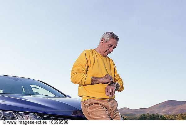 Aged traveler checking time near car