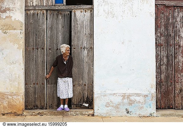 Aged woman at the entrance door of her house with a decayed fa?ade of crumbling plaster and weathered wooden doors. Remedios  Cuba.