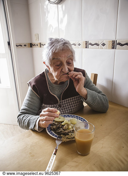 Aged woman eating fish and potatoes in the kitchen