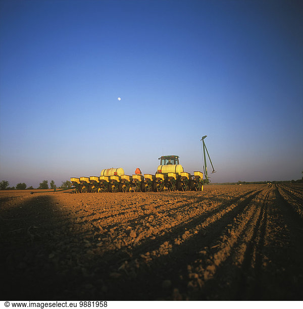 Agriculture - Rear view of a John Deere tractor and 12-row planter planting grain corn in a conventionally tilled field in late afternoon light / Ontario  Canada.