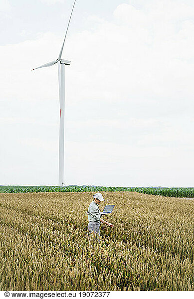Agronomist examining crops in front of wind turbine at field