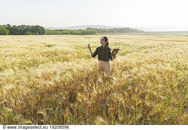 Agronomist gesturing and examining wheat crops with tablet PC at field