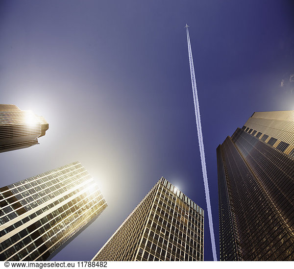 Airplane and vapor trail in blue sky above highrise buildings  travel concept