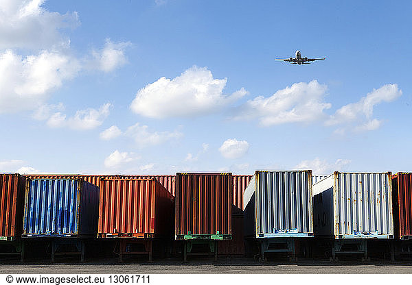 Airplane flying over cargo containers against sky