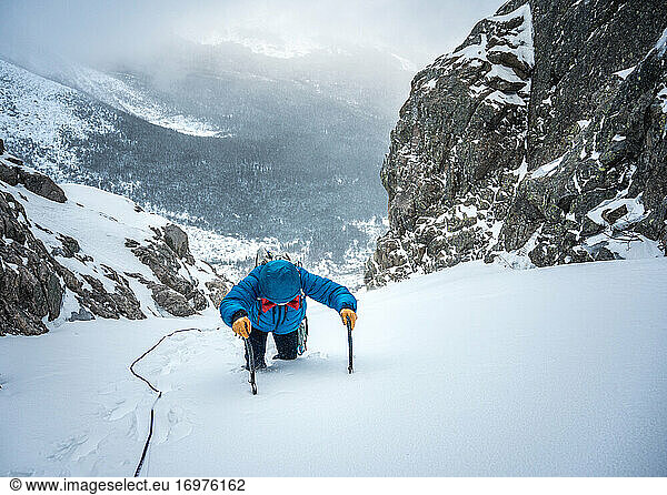 Alpinkletterer schraubt sich beim Eisklettern eine steile Schneepassage hoch