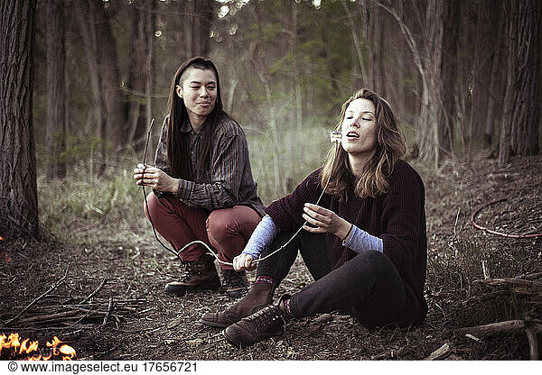 alternative female friends eating marshmallows by the fire in forrest