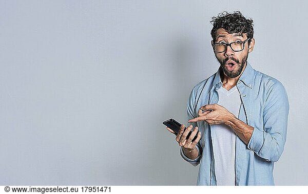 Amazed handsome man pointing at his cell phone isolated  surprised person pointing at his cell phone isolated. Isolated teenager surprised of a promotion on his cell phone