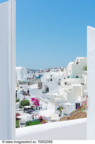 amazing panoramic view through a gate of some white houses of the village of touristic Oia in Santorini island in Aegean sea. Many tourists at the back are visiting a spectacular place. Verti