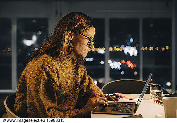 Ambitious businesswoman using laptop while working late at creative office