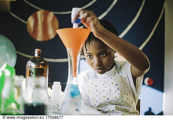 Ambitious girl mixing chemical solution while learning science project at table