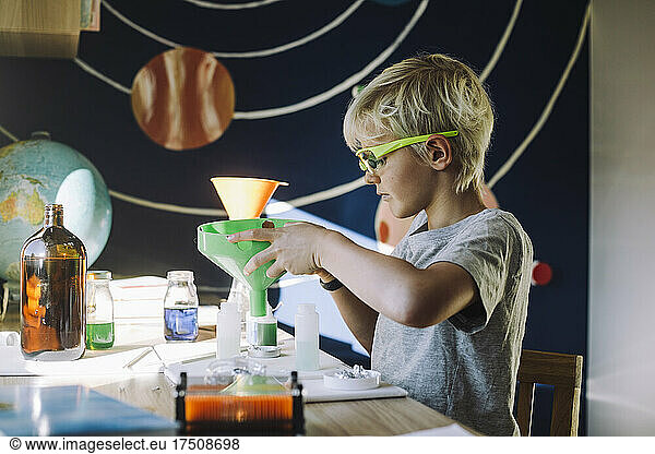 Ambitious male student mixing chemical through funnel at table