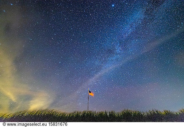 American flag waving in the night sky under the Milky Way galaxy.