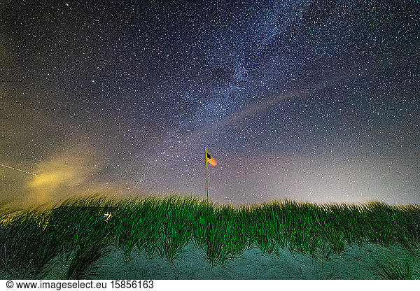 American flag waving in the night sky under the Milky Way galaxy.