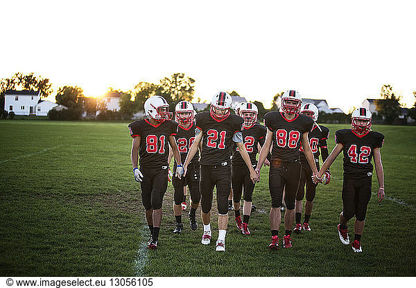 American football team holding hands while walking on field against sky