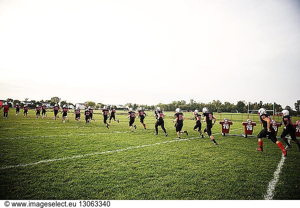 American Football team running on grassy field against sky
