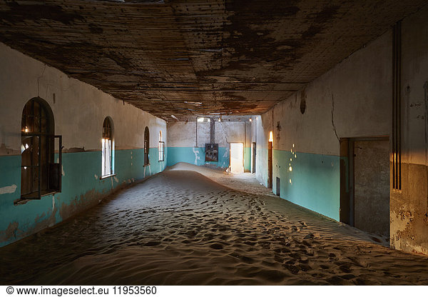 An abandoned building with boarded up windows  and shafts of sunlight lighting up the drifting sands and remnants of wall coloured green.