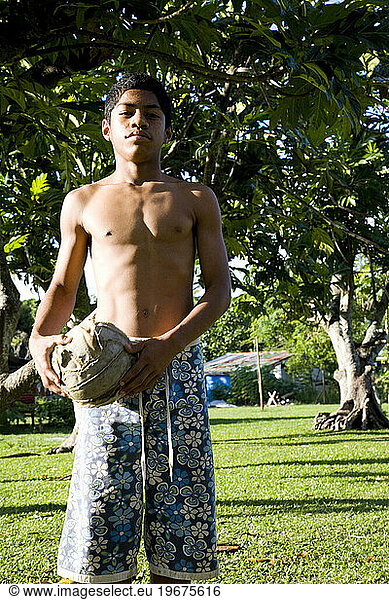 An adolescent boy stands with a beat up ball in hand at dusk.