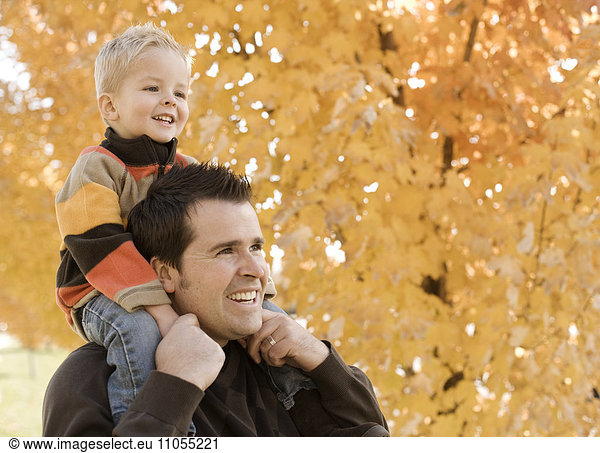 An adult parent and child  father and son under a canopy of orange autumn leaves.