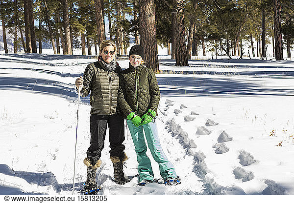 An adult woman and teenage girl in snow shoes in woodland holding ski poles