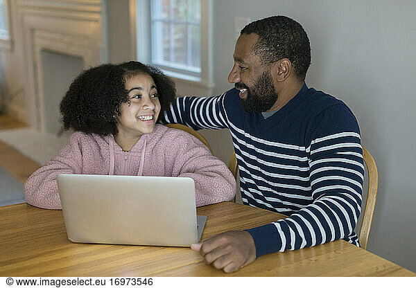 An African-American father and tween daughter smile at each other