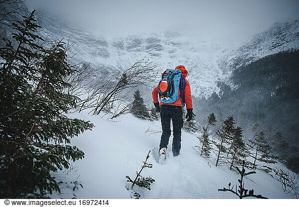 An alpine climber walks through blowing snow while headed to a climb