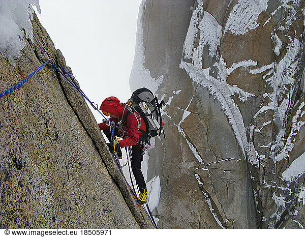 An alpinist climbs on the north face of Punta Herron  with the ice-coated granite wall of Cerro Standhardt in the background.