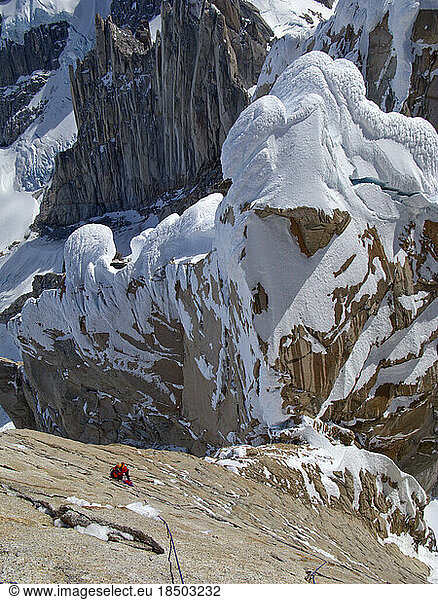 An alpinist climbs up the steep north face of Torre Egger  with the snowy west ridge of Punta Herron in the background below.