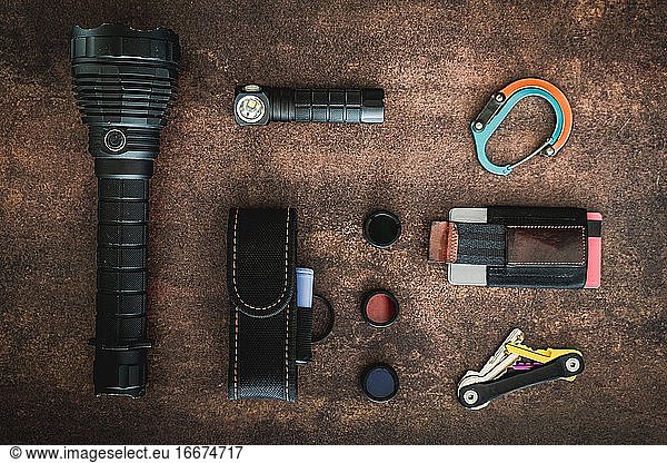 An amount of some EDC (Everyday carry) items on a wooden surface. There are some flashlights  a clip  a minimalist wallet  3 flashlight filters  a flashlight cover and a key organizer keychai