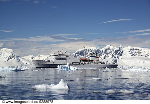 An Antarctic cruise ship with inflatable zodiacs on the calm waters among ice floes and mountainous landscape.