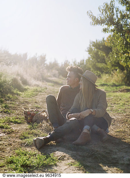 An apple orchard in Utah. A couple sitting on a sunlit path.