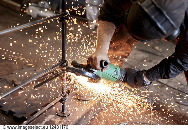 An artisan metalworker at work holding an angle grinder  working on a metal fence.
