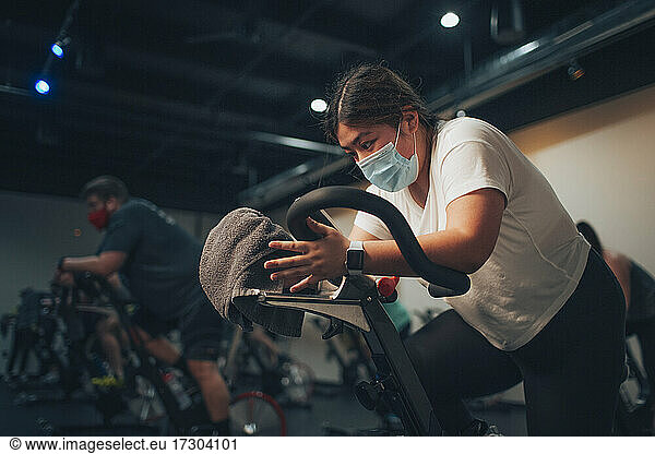 An asian woman pedals on a stationary bike in an indoor bike studio.