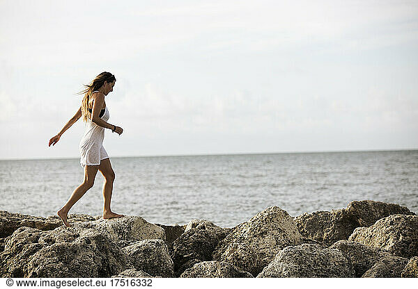 An attractive woman walks barefoot across jetty at the water edge