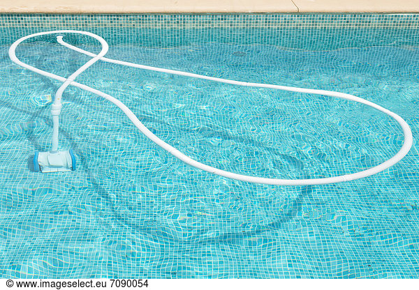 An automatic pool cleaning device attached to a hose floating in a swimming pool  lined with blue tiles